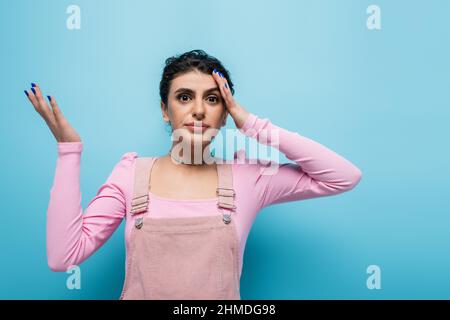 donna scoraggiata e scoraggiata che tocca la testa mentre guarda la fotocamera su sfondo blu Foto Stock