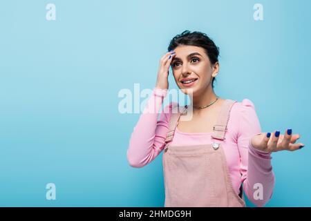 donna dimenticante che tocca la testa e punta con la mano mentre pensa isolato su blu Foto Stock
