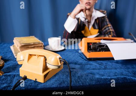 vista parziale del newswoman sfocato vicino al telefono vintage, la macchina da scrivere e libri su tovaglia velluto blu Foto Stock