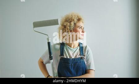 Capelli ricci caucasici satisfyied con vernice a rullo che si affaccia intorno in camera appena panificata. Foto di alta qualità Foto Stock