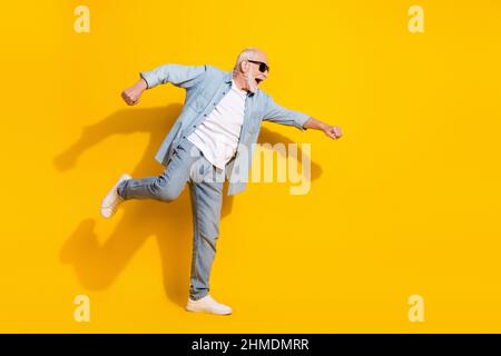 Vista a tutta lunghezza del corpo di attraente allegro motivato uomo grigio-capelli avendo divertimento isolato su sfondo di colore giallo lucido Foto Stock