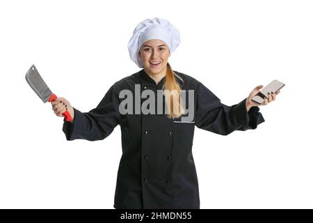 Giovane donna eccitata, cuoca, cuoco in uniforme nera isolato su sfondo bianco. Cucina, professione, affari, cibo, gusto, concetto di ristorante. Foto Stock