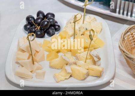 Piatto di formaggi su un tavolo bianco. Molti tipi di formaggio su un piatto con uva rossa servita. Foto Stock