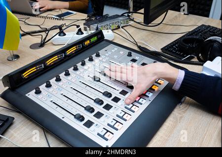 Mano di un sound man che regola il livello del suono su un mixer audio da studio presso lo studio radio Foto Stock