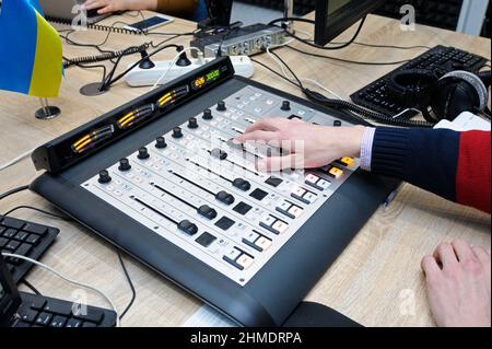 Mano di un sound man che regola il livello del suono su un mixer audio da studio presso lo studio radio Foto Stock