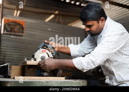 Focus su macchina, carpentiere indiano lucidare il legno utilizzando strumenti di Falegnameria in officina - concetto di lavoro autonomo, piccole imprese e lavoratori autonomi. Foto Stock