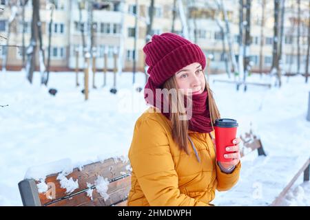 Passeggiata invernale in una città nevosa. Una giovane donna gode di una tazza di caffè caldo in inverno Foto Stock