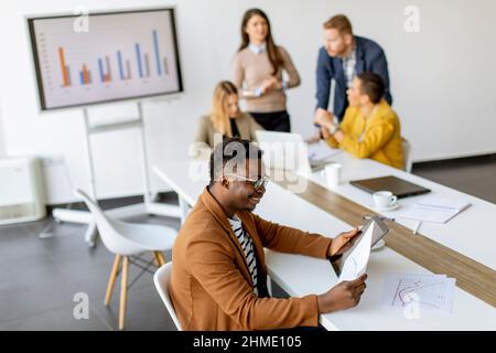 Bel giovane uomo d'affari afroamericano che lavora con un tablet digitale davanti ai suoi colleghi nella sala riunioni Foto Stock