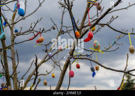 Molte uova di Pasqua decorate all'aperto. casa fai da te artigianale decorazione esterna con uova di pasqua colorate appese su albero ramificazioni primavera. Creatività artigianale Foto Stock