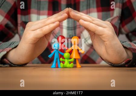 Concetto di assicurazione di famiglia con figurine di famiglia colorate coperte da mani su un tavolo di legno. Sicurezza e supporto Foto Stock