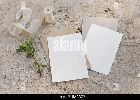 Set di mock-up con cancelleria estiva. Biglietti d'auguri vuoti, inviti e buste artigianali. Ramo di lentisco verde, nastro di seta. Calcestruzzo beige, pietra di sabbia Foto Stock