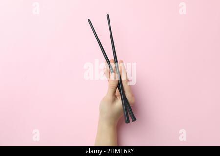 La mano femmina tiene i bacchetti su sfondo rosa Foto Stock