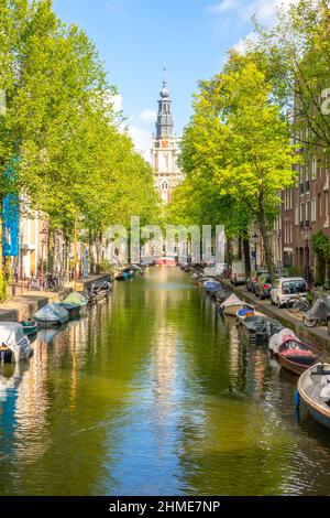 Paesi Bassi. Giornata estiva soleggiata sul canale di Amsterdam. Auto parcheggiate sul argine e molte barche ormeggiate sull'acqua. Edificio della Cattedrale in dist Foto Stock