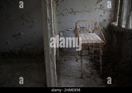 Letti abbandonati in un vivaio in un ospedale in decadenza a Pripyat, Ucraina, vicino alla centrale nucleare di Chernobyl. Foto Stock