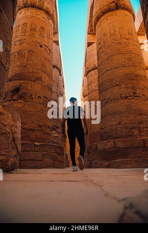 Colpo verticale di uomo turistico a piedi intorno alle colonne massicce nel tempio di luxor in egitto. Qui, dopo migliaia di anni, sorgono antiche colonne egiziane Foto Stock