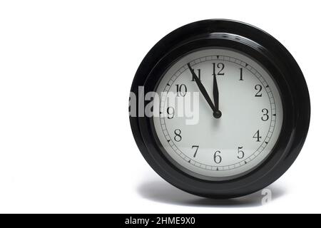 Primo piano del classico orologio analogico nero con quadrante bianco e mani scure che mostrano da cinque a dodici su sfondo bianco concetto per l'orario di appuntamento e chiamata Foto Stock