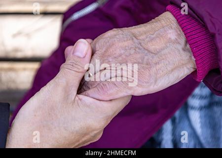 Una donna matura tiene la mano della madre anziana mentre siedono su una panca Foto Stock