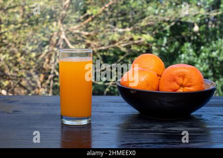 Succo di mandarino appena spremuto in un bicchiere con una ciotola di mandarini non sbucciati. Foto Stock