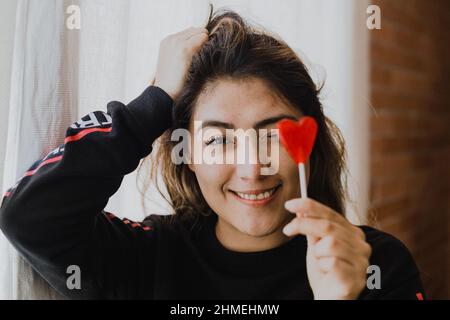 Donna latina innamorata di un lecca in mano a forma di cuore. San Valentino Foto Stock