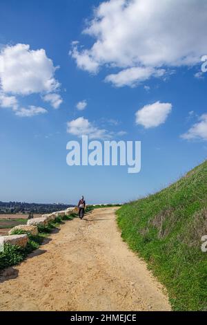 una ragazza cammina lungo una strada gialla su una collina sotto un cielo blu con nuvole bianche Foto Stock