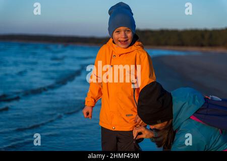 Un ragazzo e sua madre camminano lungo la baia in una serata autunnale al tramonto, tempo di famiglia all'aperto. Foto Stock