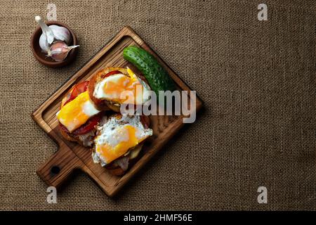 Sandwich fatti in casa con carne, patate, pomodoro, cetrioli, uova fritte, aglio, su un asse di legno Foto Stock