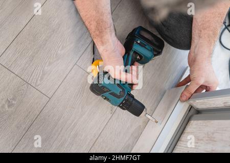 Un uomo sconosciuto maschio caucasico usando il trapano avvitatore elettrico senza fili che monta i mobili a casa DIY carpentiere al lavoro primo piano su mani copia spa Foto Stock