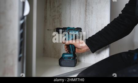 Un uomo maschio caucasico con avvitatore elettrico a batteria trapano montaggio mobili a casa DIY carpentiere al lavoro Foto Stock