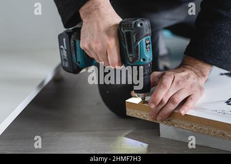 Un uomo sconosciuto maschio caucasico usando il trapano avvitatore elettrico senza fili che monta i mobili a casa DIY carpentiere al lavoro primo piano su mani copia spa Foto Stock