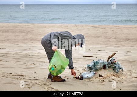 il volontario maschile raccoglie i detriti gettati da una tempesta su una spiaggia sabbiosa Foto Stock