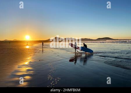 Surfers sulla spiaggia di Caleta de Famara al tramonto, Lanzarote, Spagna Foto Stock