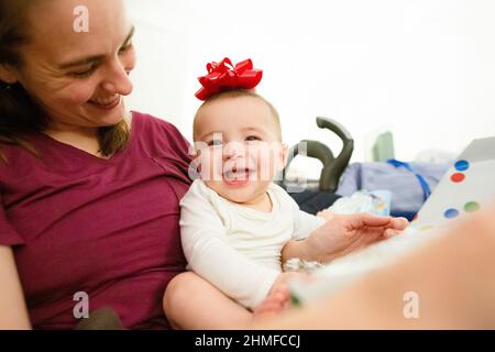 Happy Baby si siede nel Lap della mamma sorridendo con l'arco rosso sulla testa Foto Stock