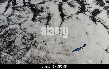 Vista aerea di uomo e cane in piedi su un lago ghiacciato di neve. Foto Stock