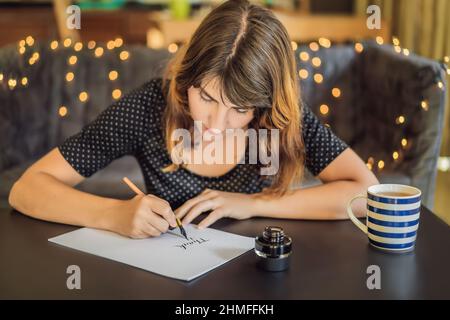La ringrazio. Calligrapher giovane donna scrive una frase sul libro bianco. Inscrivendo ornamentali in lettere decorate. La calligrafia, graphic design, scritte Foto Stock