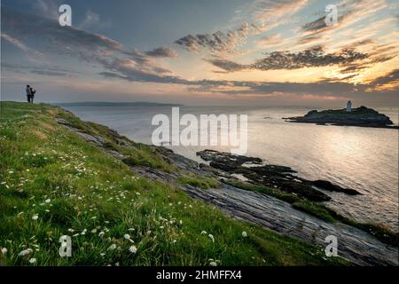 Godrevy, North Cornwall, Inghilterra-Luglio 22nd 2021:a metà estate, i visitatori di questo famoso punto di riferimento, puntano i loro telefoni al tramonto del sole e del faro dell'isola Foto Stock