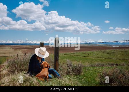 Donna e leale cocker spaniel condividere un momento insieme in un campo insieme con le montagne Teton sullo sfondo. Foto Stock