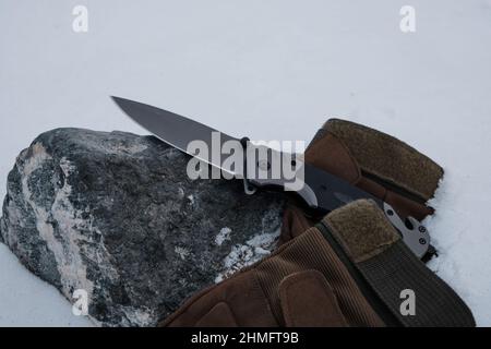 Guanti tattici e un coltello pieghevole nella neve Foto Stock