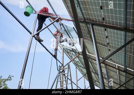 Lavoratori che installano pannelli solari fotovoltaici all'aperto. Elettricisti uomini che collocano il modulo solare su guide metalliche. Energia rinnovabile ed ecologica. Foto Stock