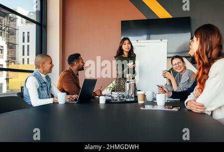 Giovane donna d'affari che fa una presentazione in una sala riunioni. Donna d'affari intelligente che presenta la sua strategia aziendale ai suoi colleghi. Gruppo di multirazziale Foto Stock