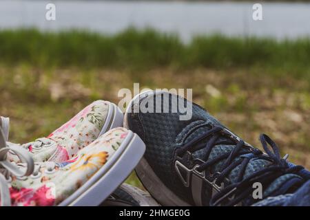 Le gambe di una giovane donna e di un uomo si calzano con scarpe da running. Riposatevi sul sentiero turistico sulla riva del fiume Foto Stock