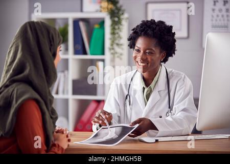 Dottore o consulente femminile che ha avuto un incontro con il paziente femminile che indossa il foulard per discutere le scansioni Foto Stock