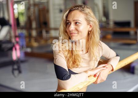 Poirtrait di attraente giovane donna, ballerino in piedi vicino balletto barre in studio stretching Foto Stock