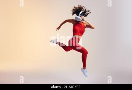 Giovane donna sportiva che si sprint indossando un visore per realtà virtuale. Giovane atletica che corre durante una sessione di allenamento virtuale. Donna che lavora Foto Stock