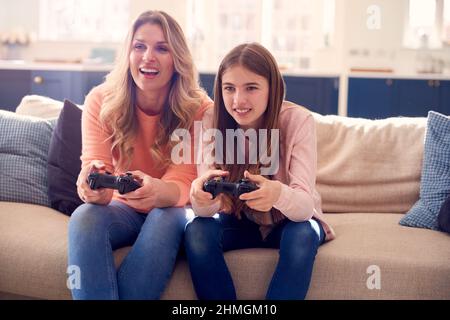 Madre e figlia che hanno divertimento seduto sul divano a casa giocando sulla console di gioco Foto Stock