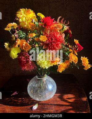 Bouquet romantico e luminoso di dahlias e crisantemi colorati in un vaso di vetro sul tavolo ai raggi del sole Foto Stock