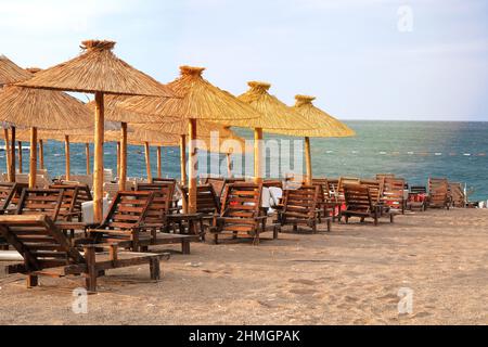 Ombrelloni di paglia su idilliaco resort tropicale. Mare blu e cielo con luce solare giallo tenue. Foto Stock