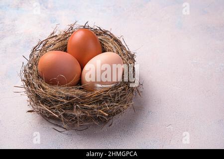 Tre uova di pollo in un nido su sfondo chiaro. Vista laterale, spazio di copia. Foto Stock
