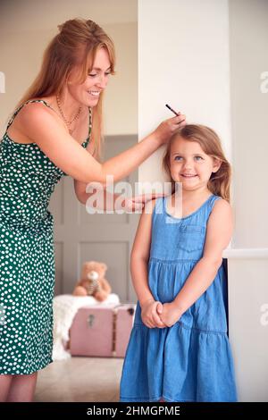 Madre che misura l'altezza della figlia e la marcatura sul muro a casa Foto Stock