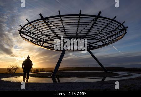 Haslingden, Lancashire, Regno Unito, mercoledì 09 febbraio 2022. Un escursionista si ferma per ammirare il sole tramontare al panopticon Halo sopra la città di Haslingden, Foto Stock