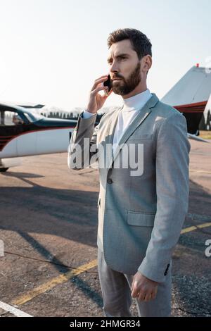 uomo d'affari bearded che ha chiamata telefonica sullo smartphone vicino elicottero all'aperto Foto Stock